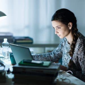 College student studying at a laptop beside a stack of books